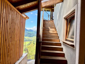 A wooden staircase leading to a balcony with a view of a mountainous landscape.