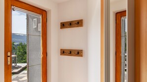 Habitació amb porta de fusta, finestra amb vista a vegetació i muntanyes, i dues ganxos de fusta penjats a la paret.
