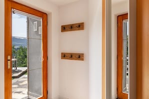 A room with a wooden door, a window with a view of greenery and mountains, and two wooden wall-mounted hooks.
