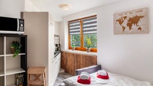 Habitación de hotel compacta con cama, una mesita pequeña, microondas, estante con una planta, ventana con persianas y un mapa mundial en la pared.