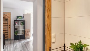 Una habitación con una puerta de madera, un estante negro con plantas, un microondas y una pared de azulejos blancos.