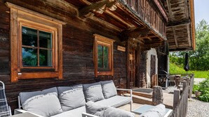 A rustic wooden cabin with a sofa and tables, a porch, and a sign reading 'Hiking Trail.' - Holiday Home "The Farm" with Mountain Views, Private Terrace & Wi-Fi (Westendorf)