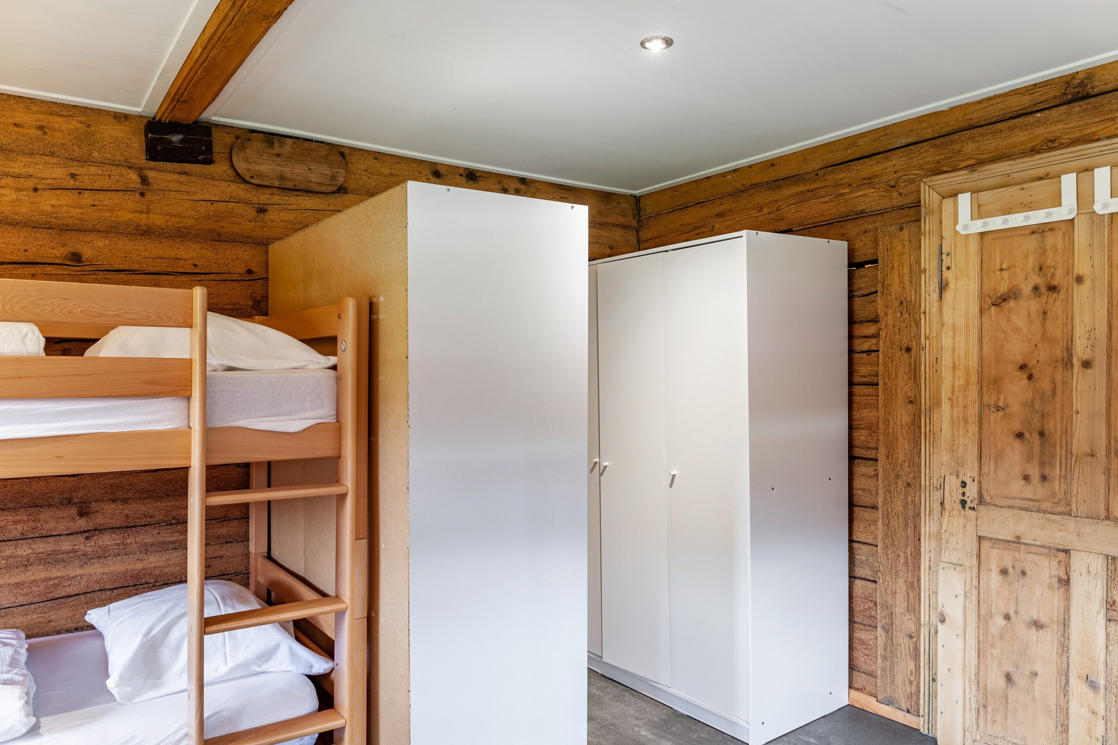 A bunk bed with white bedding, a white wardrobe, and wooden walls.