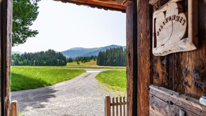 A rustic wooden door with a sign, a gravel path, and a view of a green landscape with trees and hills. - Holiday Home "The Farm" with Mountain Views, Private Terrace & Wi-Fi (Westendorf)