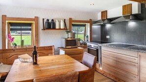 A kitchen with wooden cabinetry, a built-in microwave, a stove, and a window with a view of greenery. - Holiday Home "The Farm" with Mountain Views, Private Terrace & Wi-Fi (Westendorf)