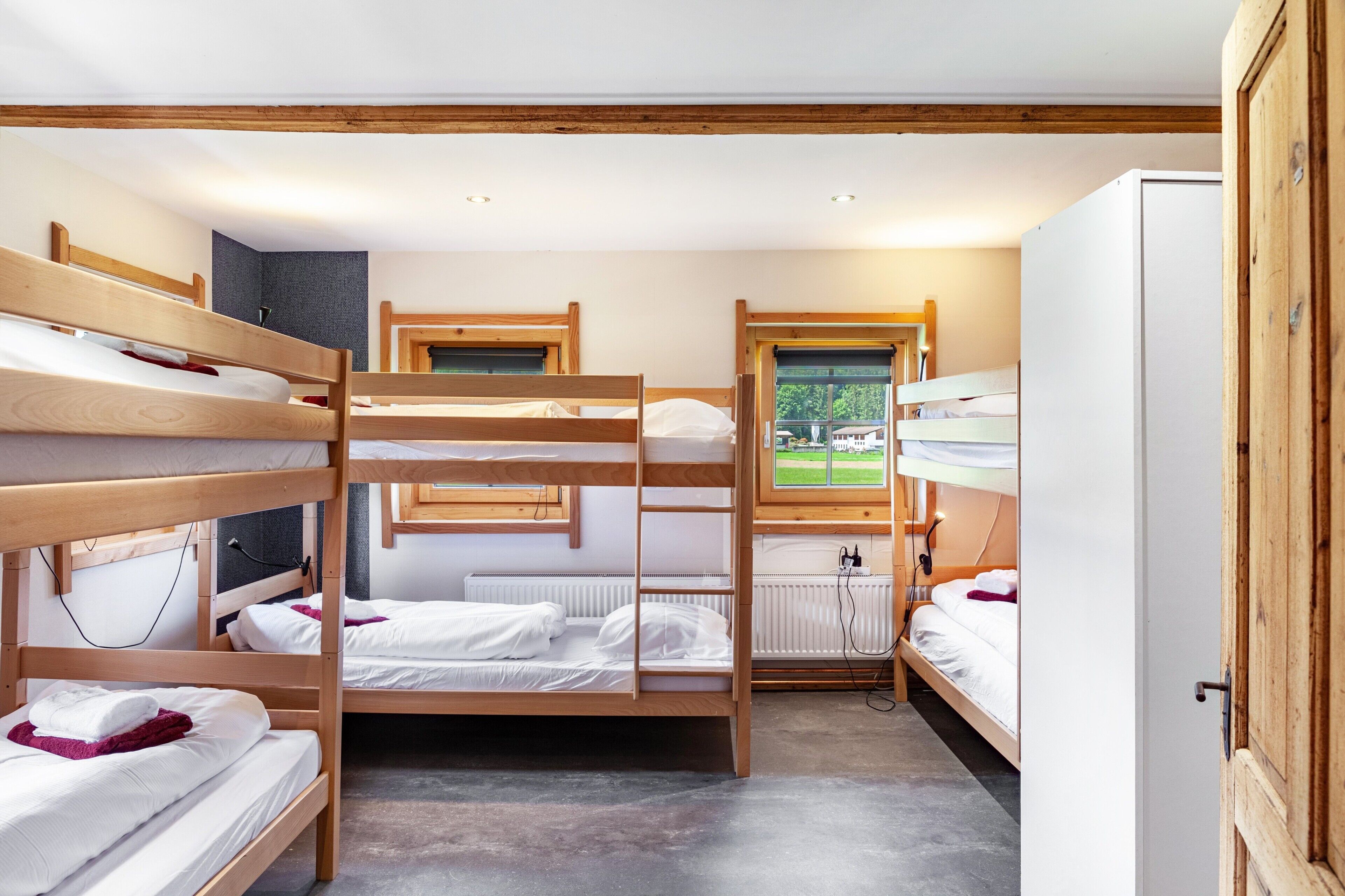 Dormitorio con literas, vigas de madera, radiador y ventana con vistas.