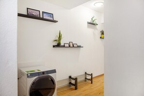Ein Waschbereich mit Waschmaschine, Pflanzenregalen und gerahmten Bildern an der Wand.
