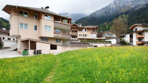 Un edificio residencial de varios pisos con balcones, un campo cubierto de flores amarillas y un telón de fondo montañoso.