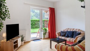 Una sala de estar con sofá, una mesa de centro, televisor sobre un mueble bajo y puerta corrediza de vidrio que da a un área exterior.