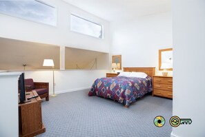 A bedroom with a bed, a desk, a chair, a lamp, a mirror, and a window.