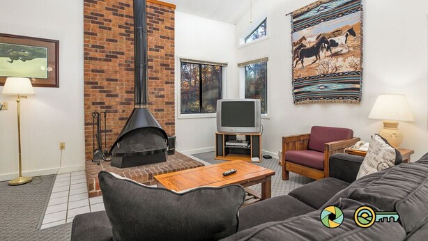 Een woonkamer met een open haard van baksteen, een televisie, een bank en een vloerkleed.