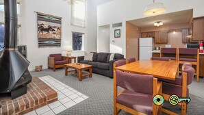 Een ruime woonkamer met een open haard, een bank, een eettafel met stoelen en een keukenhoek.