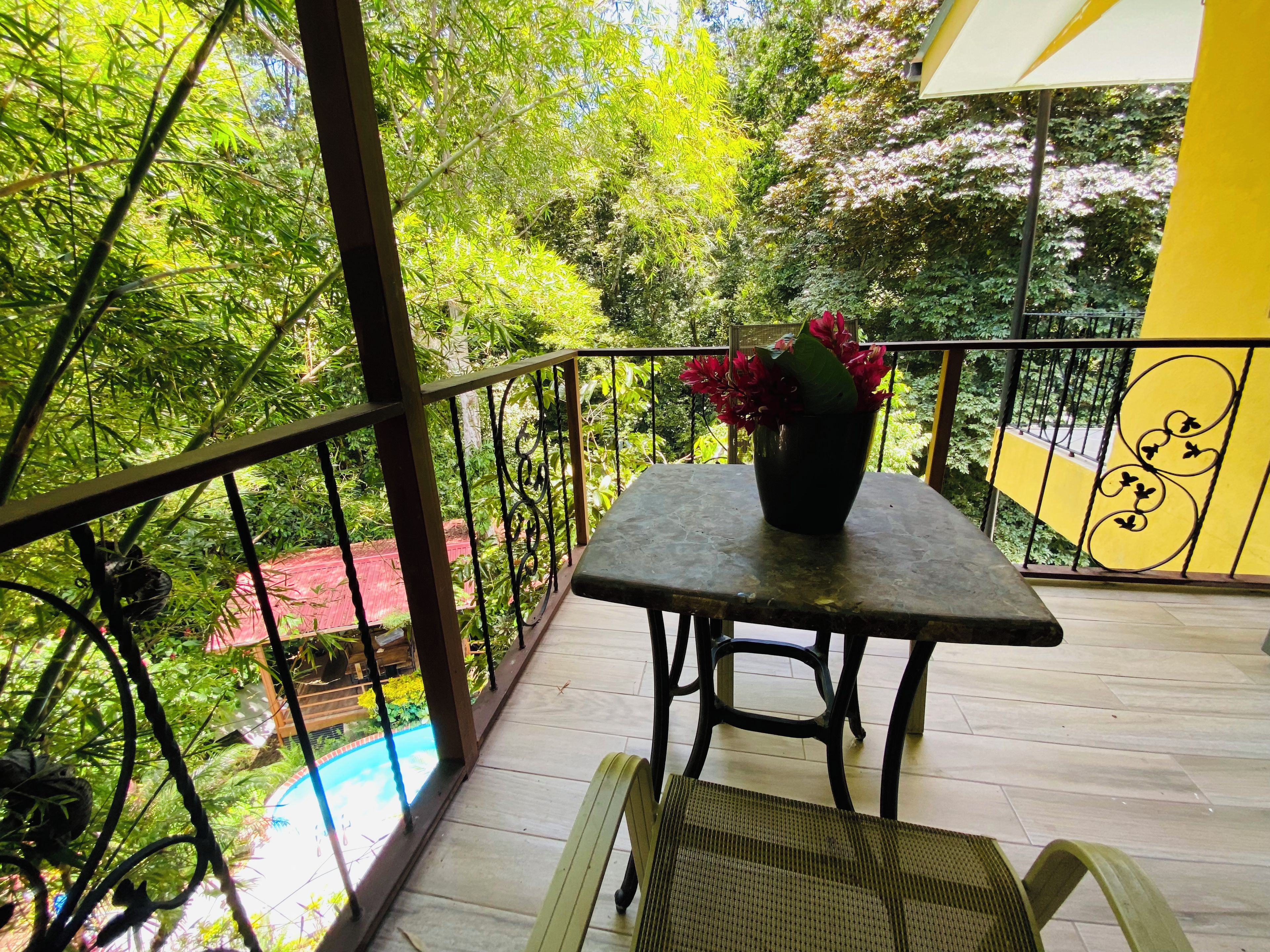 Un balcón con mesa y sillas, una planta en maceta y vista a una piscina.
