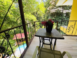 A balcony with a table and chairs, a potted plant, and a view of a swimming pool.