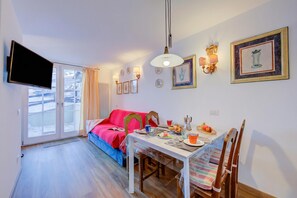 A dining area with a table set for two, a sofa, and a television mounted on the wall.