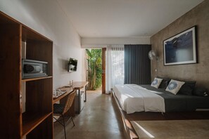 A modern bedroom with a bed, a desk, and a television. There is a view of greenery outside. - Sammy's Canggu (Canggu)
