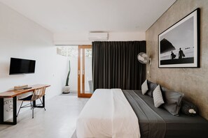 A modern hotel room with a bed, a desk, a chair, a TV, a fan, and a large framed picture on the wall. - Sammy's Canggu (Canggu)