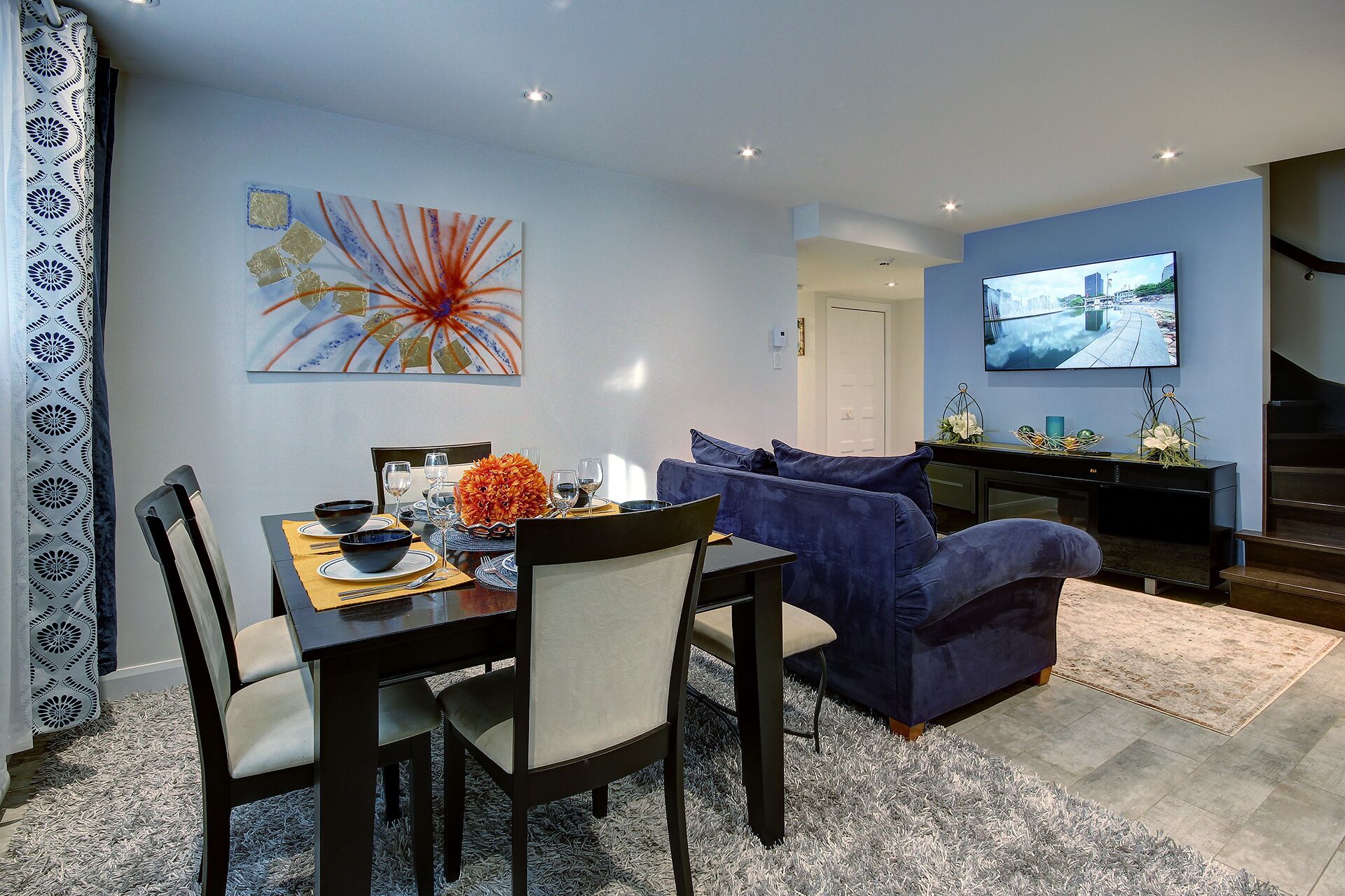 A modern living room with a dining area, featuring a sofa, a TV, and a dining table set for four.