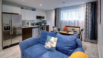 A modern kitchen with stainless steel appliances, a dining area with a table set for two, and a blue sofa with a floral pillow.