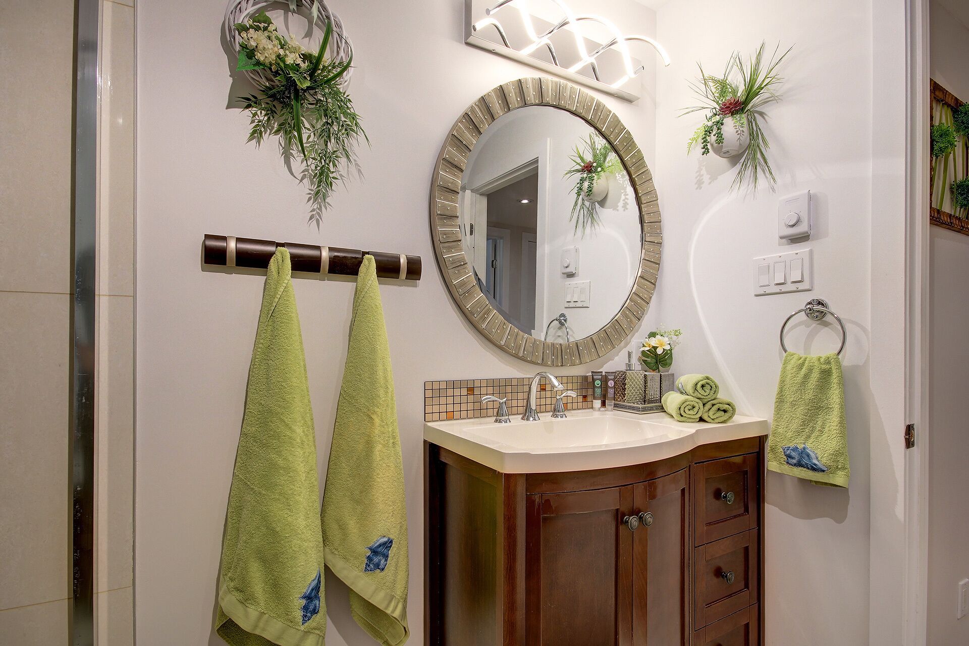 Une salle de bain avec un meuble-lavabo en bois, un miroir rond et deux serviettes suspendues à une barre à serviettes.