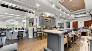 Ein modernes Restaurant mit einer zentralen Bar, hohen Decken und Blick ins Freie.