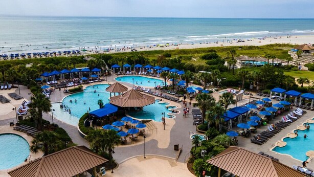 Ein Resort mit mehreren Schwimmbecken, Liegestühlen und Strand.
