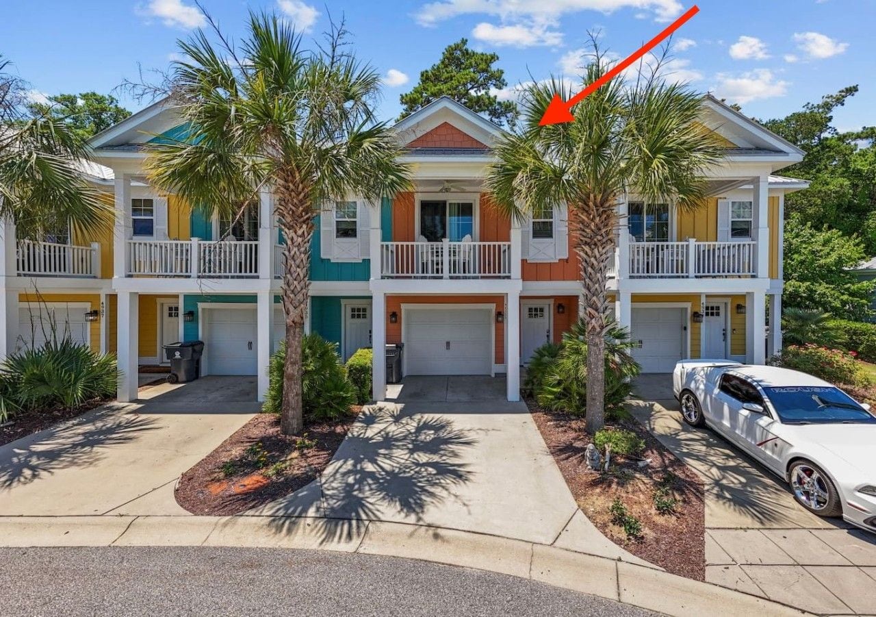 A multi-story residential building with a front porch, two garages, and a white car parked in the driveway.