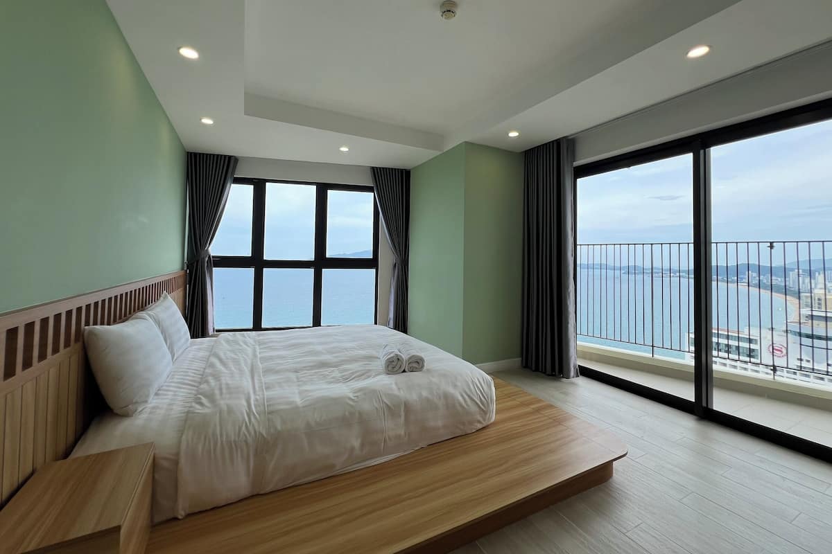 A modern bedroom with a large bed, a view of the sea, and a balcony with a railing.