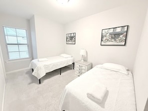 Une chambre avec deux lits simples, une table de chevet avec une lampe et deux tableaux encadrés au mur.