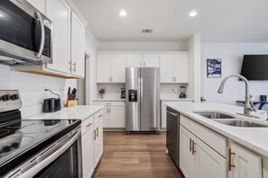 Une cuisine moderne avec des meubles blancs, des appareils en acier inoxydable et un plancher en bois.