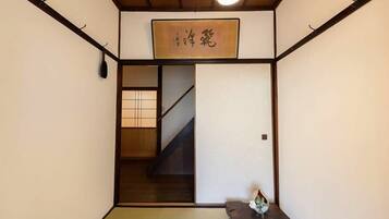 A traditional Japanese room with tatami flooring, a sliding door, a small table with a vase, and a hanging sign with Japanese characters.