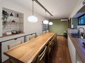 A compact kitchen with a wooden dining table, hanging pendant lights, and a built-in shelf with kitchenware. - b local Bingo Yamamo | Unique Stay in Onomichi (Onomichi)