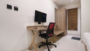 Una habitación pequeña y moderna con un escritorio de madera, una silla de oficina negra, un televisor de pantalla plana y un armario con panel acolchado.