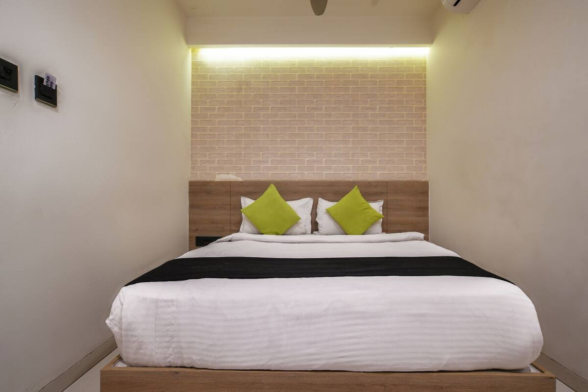 A hotel room with a brick wall, a wooden headboard, and a bed with white bedding and green pillows.