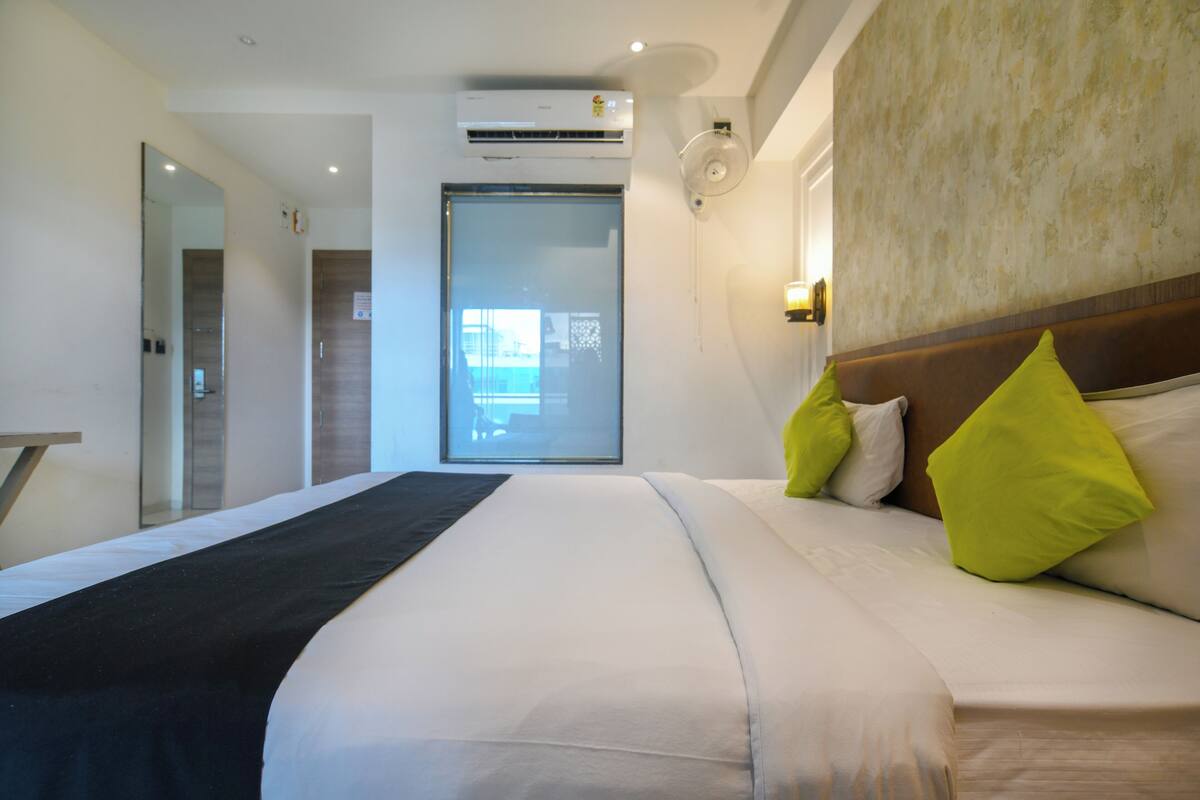 A hotel room with a large bed, a bedside table, a mirror, and an air conditioning unit.