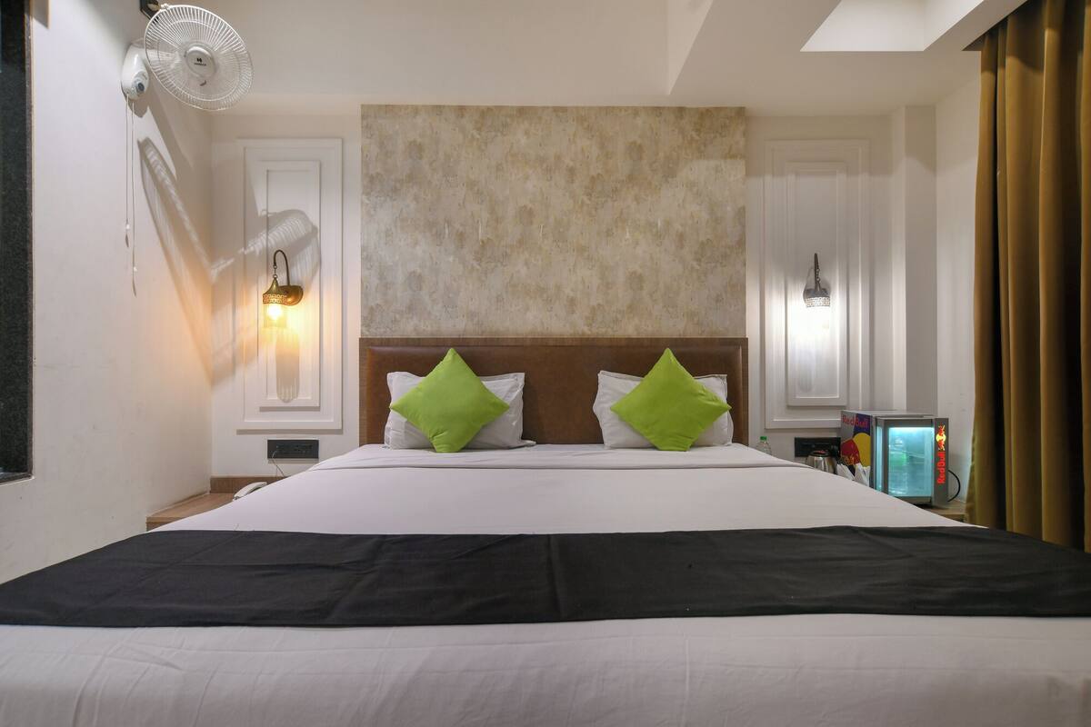A hotel room with a large bed, two green pillows, a flat-screen TV, and a wall-mounted lamp.