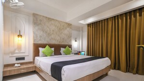 Quarto de hotel com uma cama grande, duas luminárias de cabeceira, mesa de cabeceira, luz acoplada à parede e uma janela com cortinas.