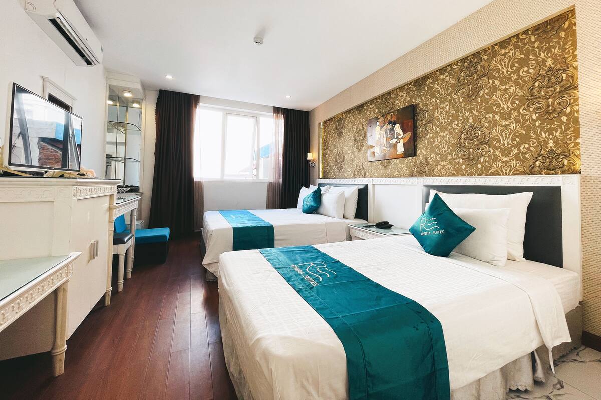 A hotel room with two beds, a desk, a TV, and a window with curtains.