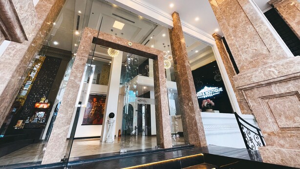 A hotel lobby with marble columns, a reception desk, and a staircase leading to the upper floor. - Rivera Boutique (Da Nang)
