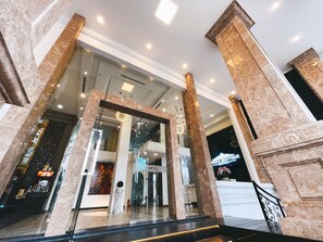 A hotel lobby with marble columns, a reception desk, and a staircase leading to the upper floor. - Rivera Boutique (Da Nang)