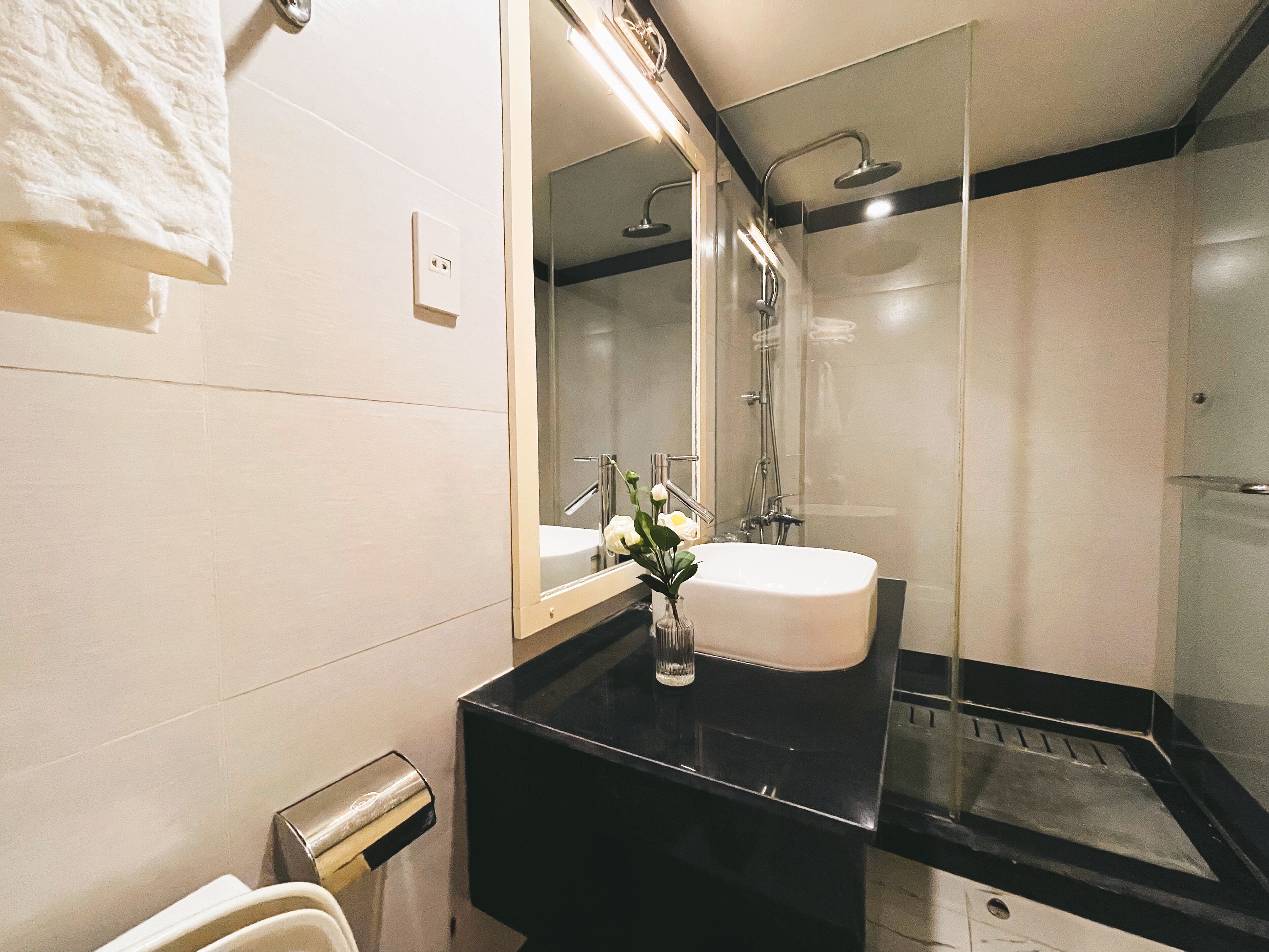 Une salle de bain moderne avec un plan de toilette noir, un lavabo blanc et une douche à parois de verre.