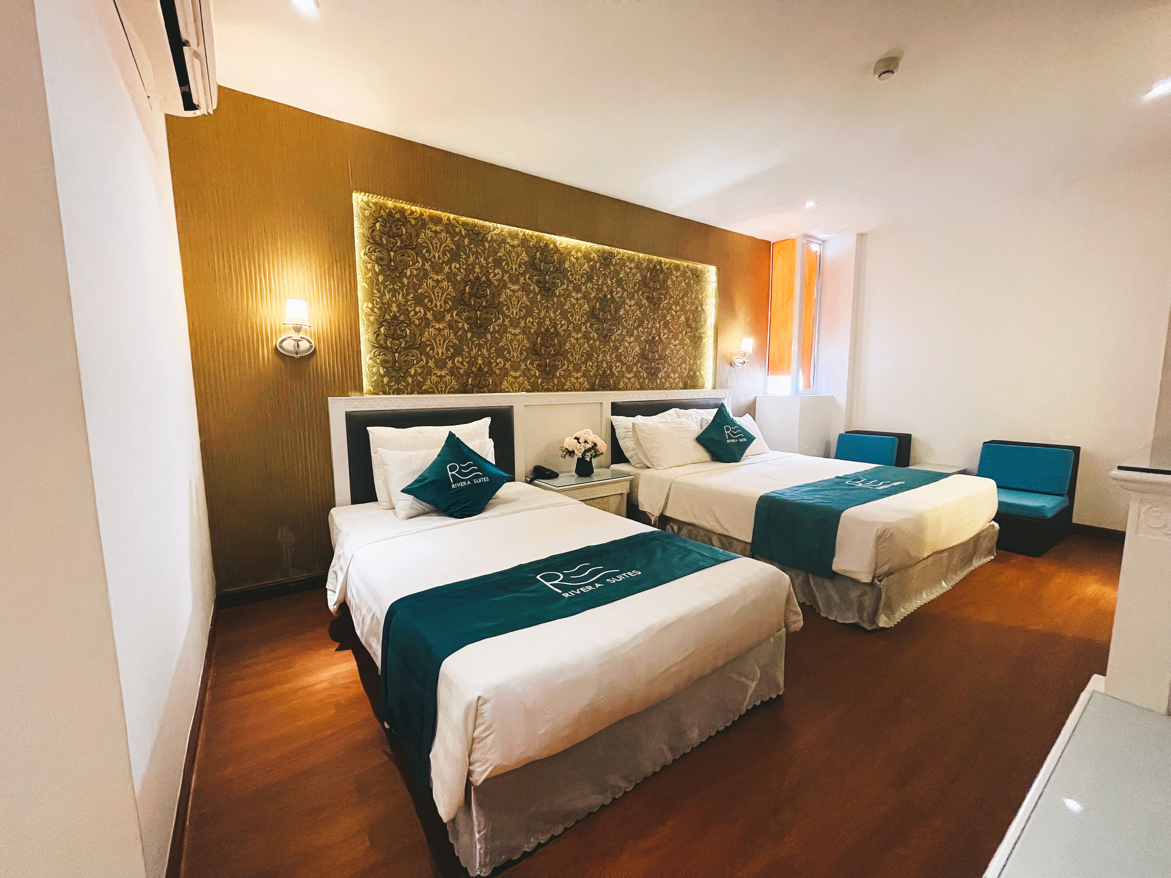 A hotel room with two beds, a wooden headboard, a decorative wall panel, and a small seating area.