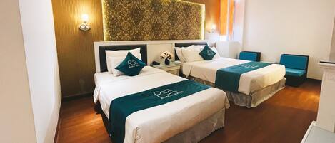 A hotel room with two beds, a wooden headboard, a decorative wall panel, and a small seating area.