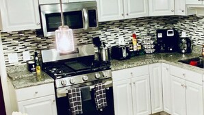 A kitchen with white cabinets, a stainless steel stove, a microwave, and a coffee maker.