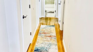 A hallway with wooden flooring, white walls, and a colorful rug.