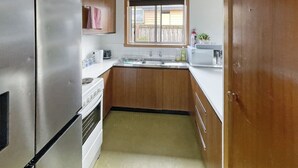 A compact kitchen with wooden cabinets, a stainless steel refrigerator, a white stove, and a window above the sink.