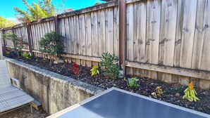 A wooden fence with a garden bed containing various plants and flowers.