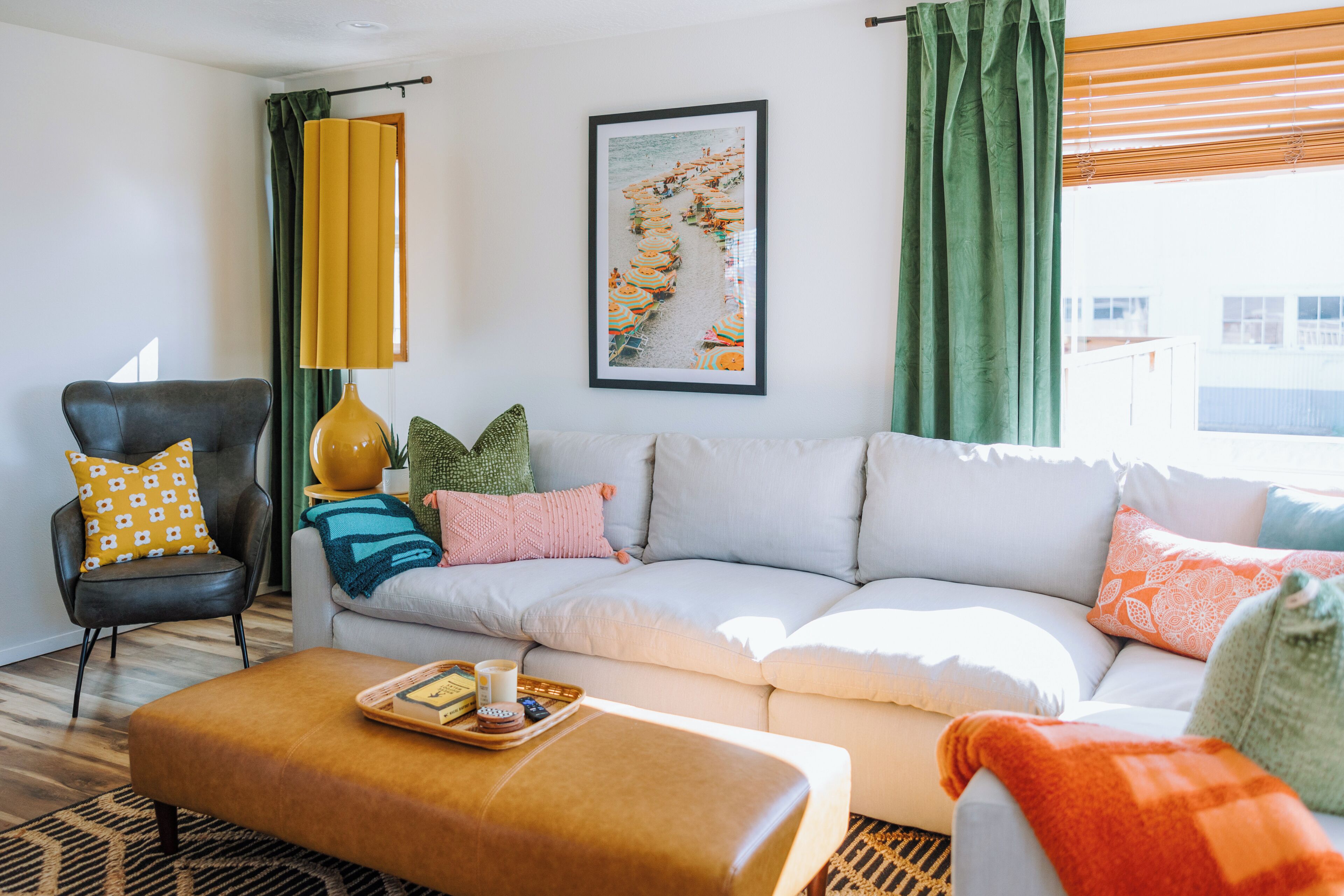 Een moderne woonkamer met een bank, fauteuil en voetenbankje, een inlijsting foto aan de muur en een raam met gordijnen.