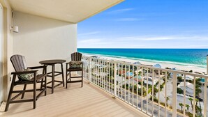 A balcony with two Adirondack chairs and a small table, overlooking a beach with a clear view of the ocean and a residential area in the distance. - Remodeled Resort Condo w/ Ocean & Beach Views (Panama City Beach)