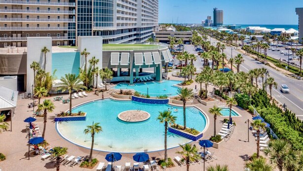 A hotel with a large central pool surrounded by palm trees and lounge chairs. - Remodeled Resort Condo w/ Ocean & Beach Views (Panama City Beach)